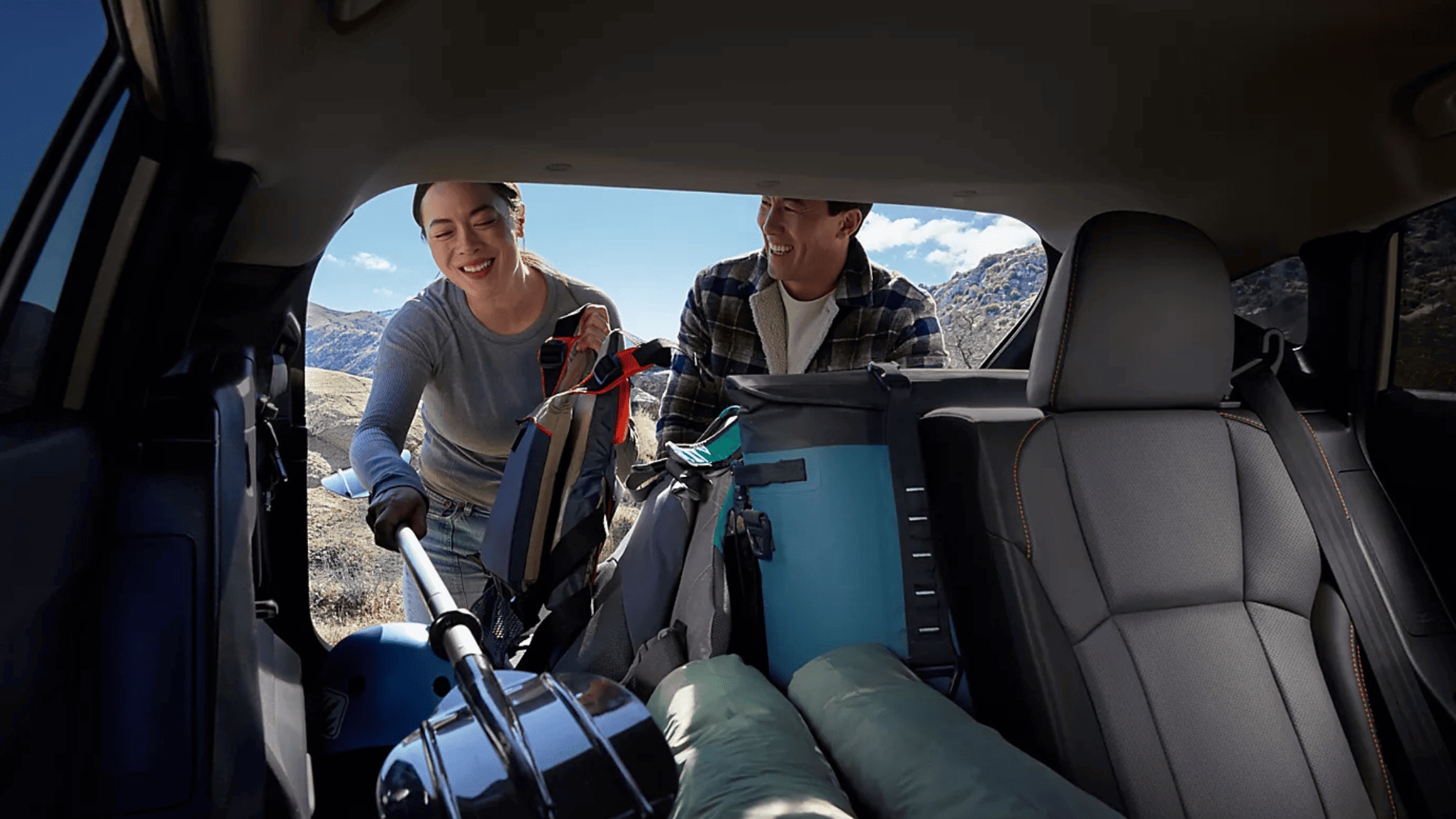 2026 Subaru Outback Wilderness cargo area loaded with camping gear including sleeping bag and trekking poles with rear hatch open in a desert setting