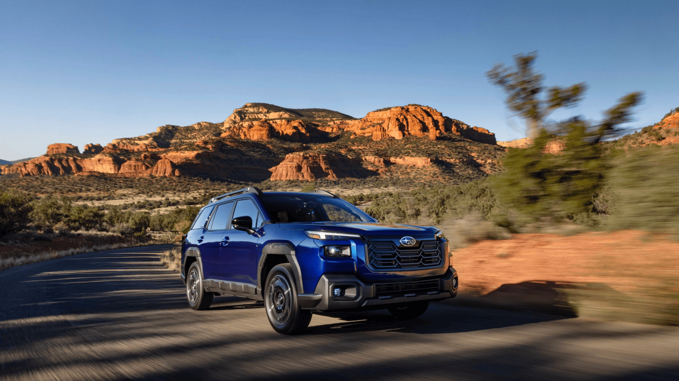 2026 Subaru Outback AWD wagon in blue driving on desert highway with red rock formations in background in Pueblo CO