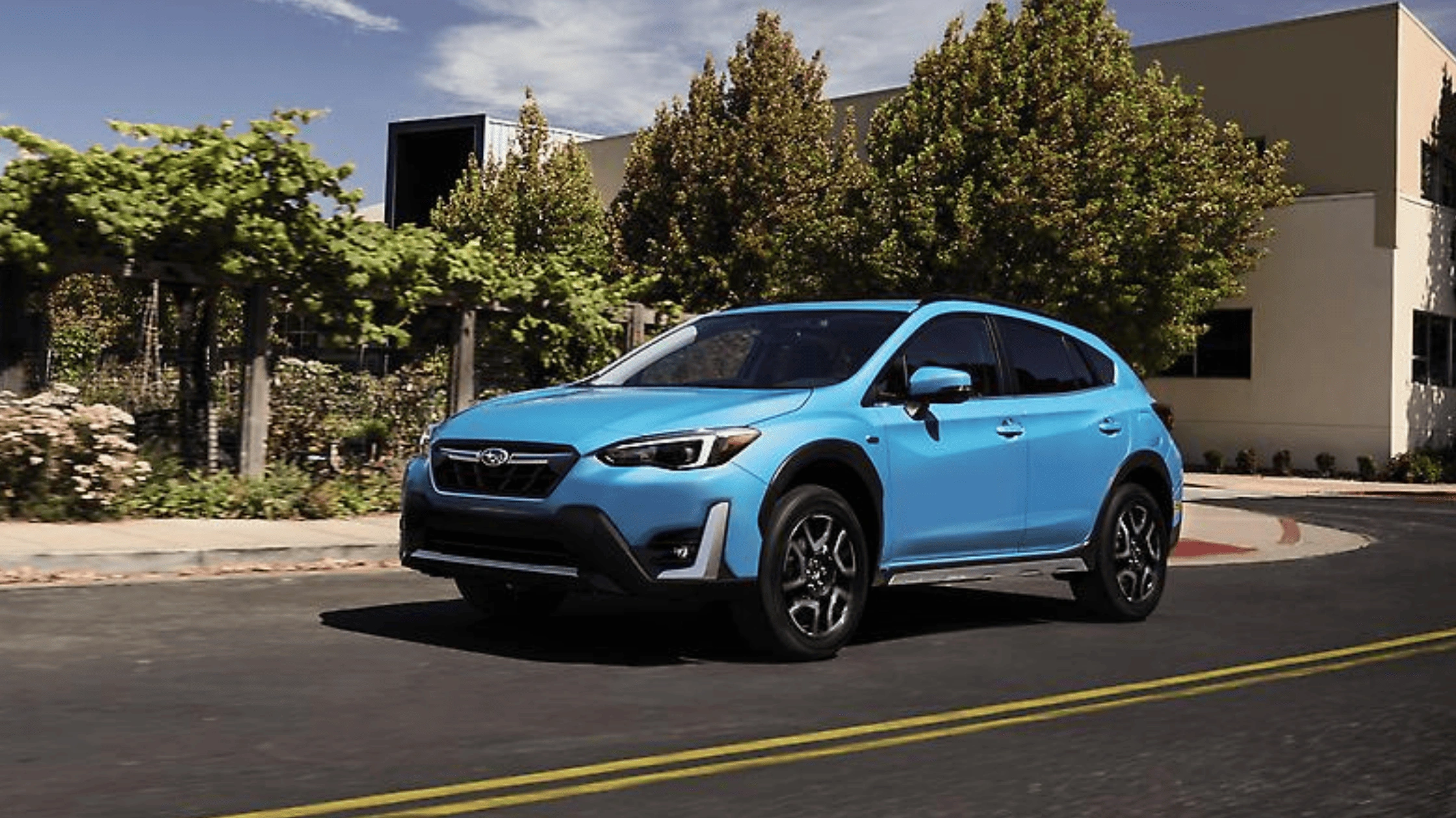2026 Subaru Crosstrek Hybrid in light blue driving through a suburban street in Pueblo, CO.