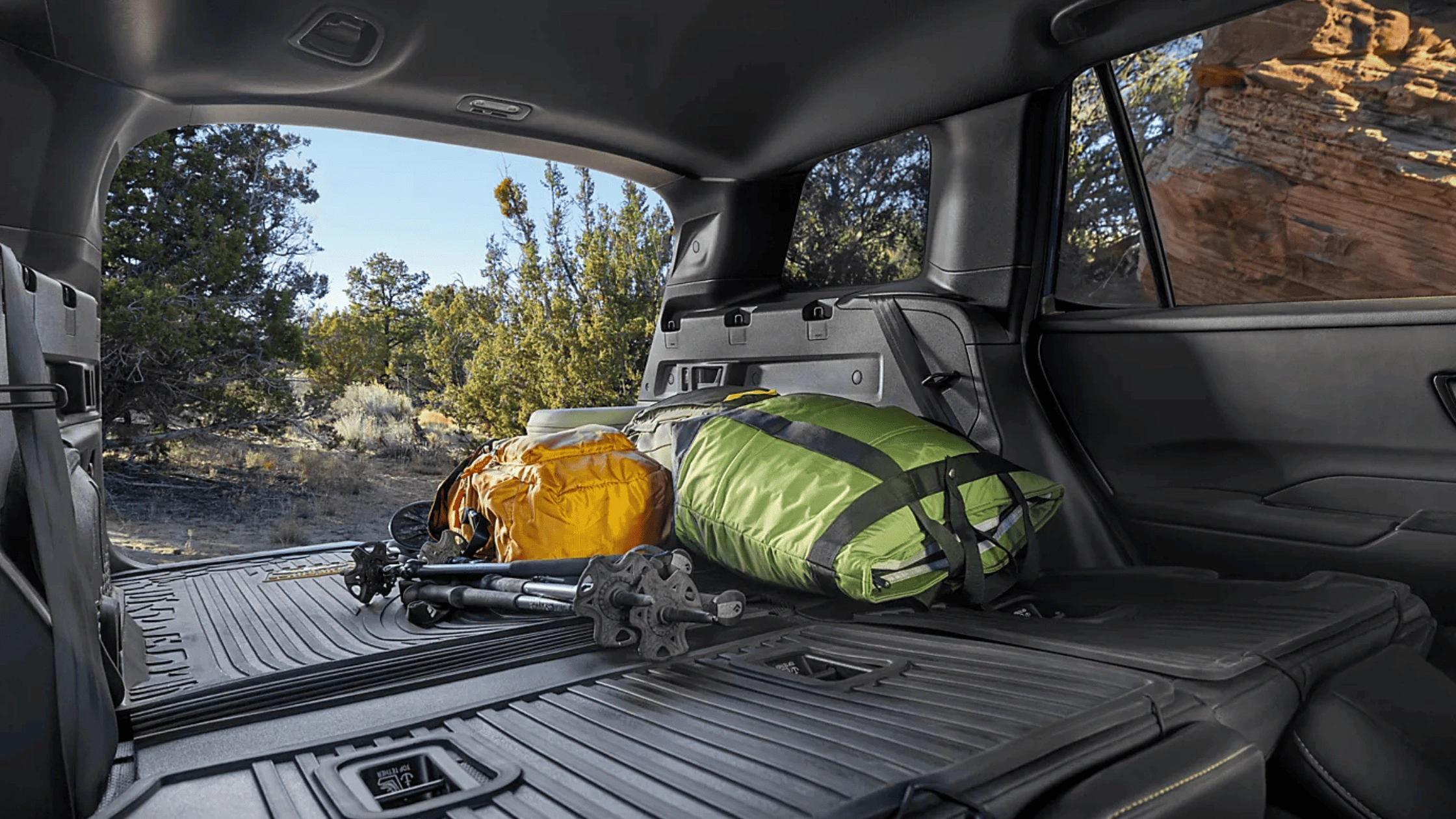 2026 Subaru Outback Wilderness cargo area loaded with camping gear including sleeping bag and trekking poles with rear hatch open in a desert setting