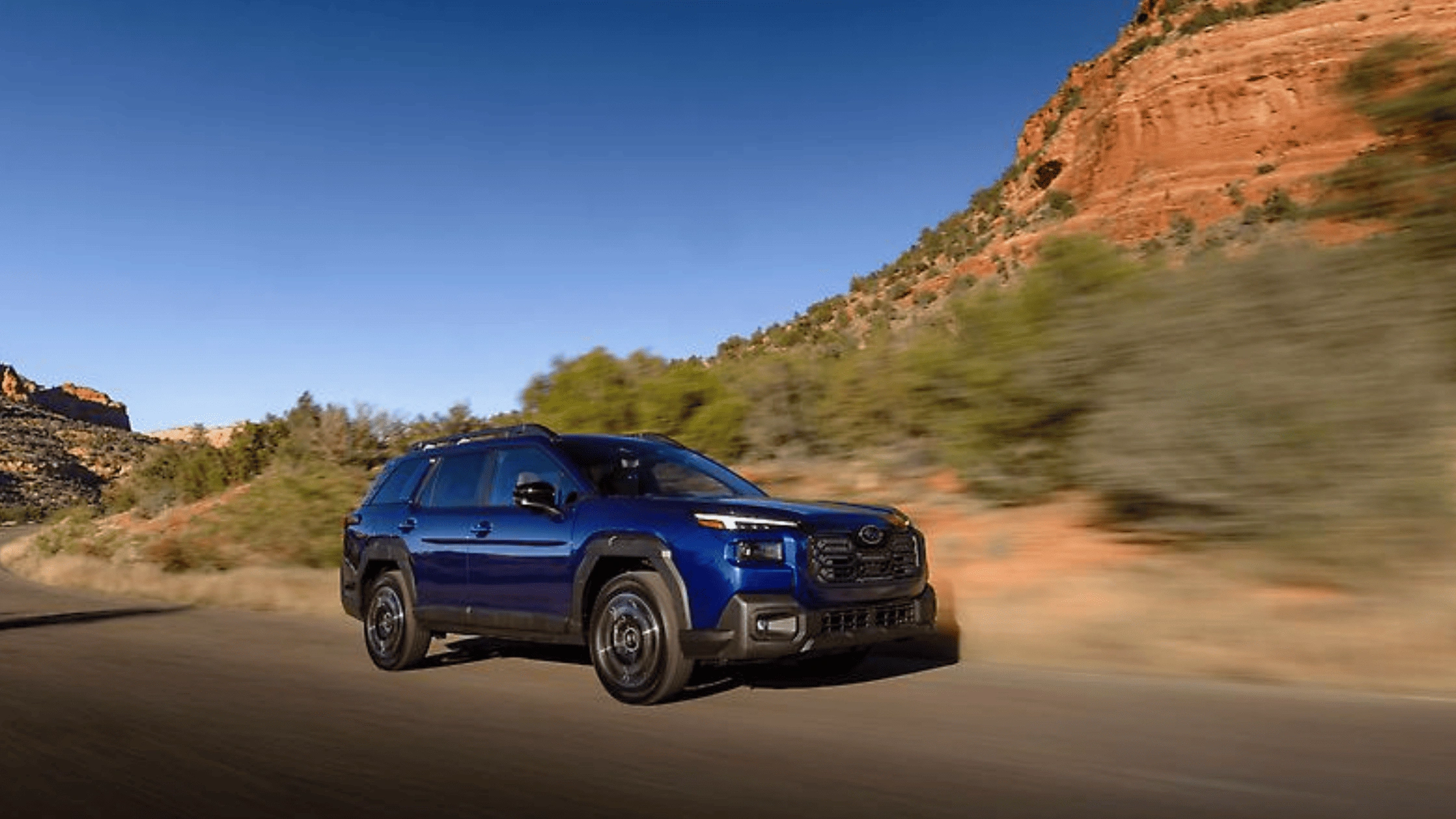 2026 Subaru Outback in blue driving on a desert road with red rock formations in Pueblo, CO.