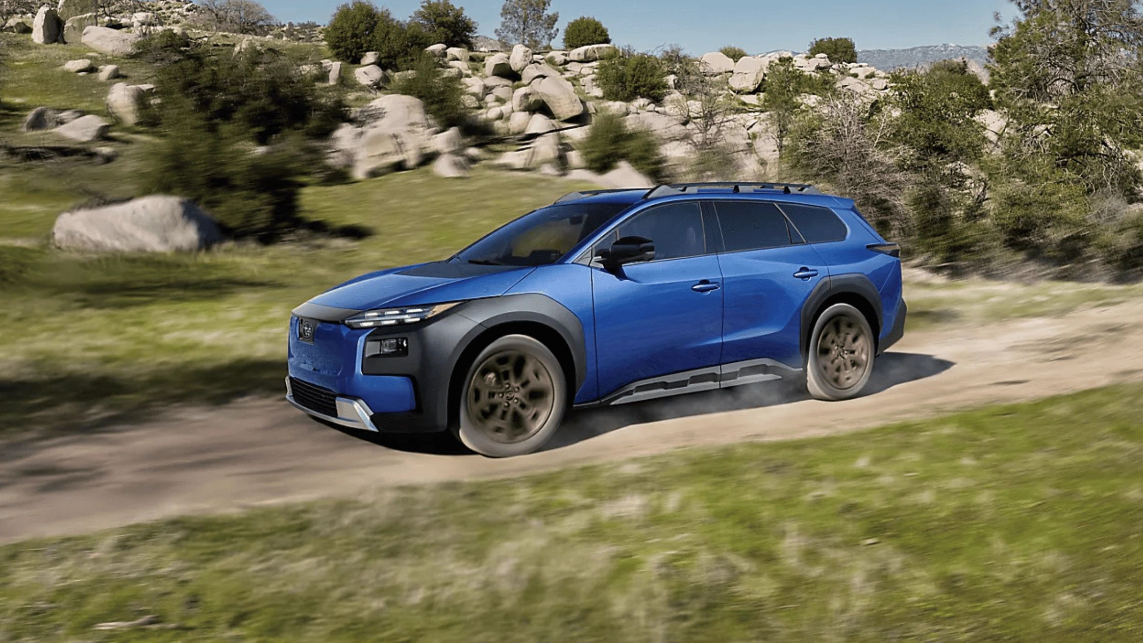 2026 Subaru Trailseeker electric SUV in blue with black cladding and roof rails driving on dusty dirt trail through rocky terrain in Pueblo CO