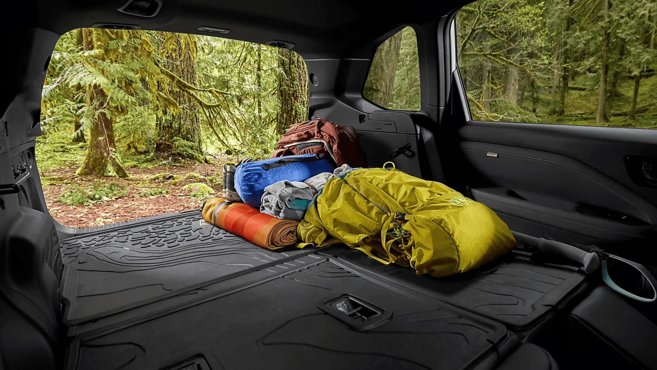 2026 Subaru Outback Wilderness cargo area loaded with camping gear including sleeping bag and trekking poles with rear hatch open in a desert setting