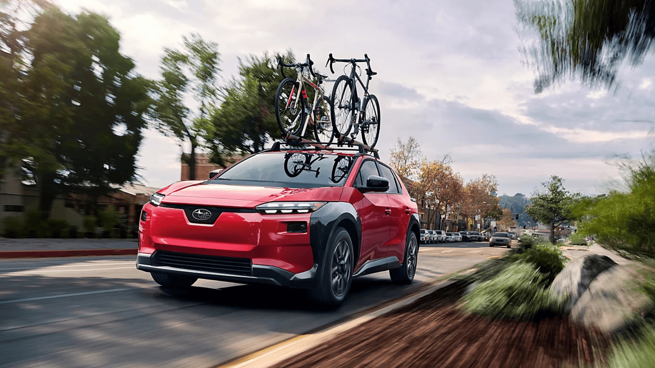 2026 Subaru Solterra electric SUV in red with roof-mounted bike rack carrying two bicycles driving through urban street in Colorado Springs CO