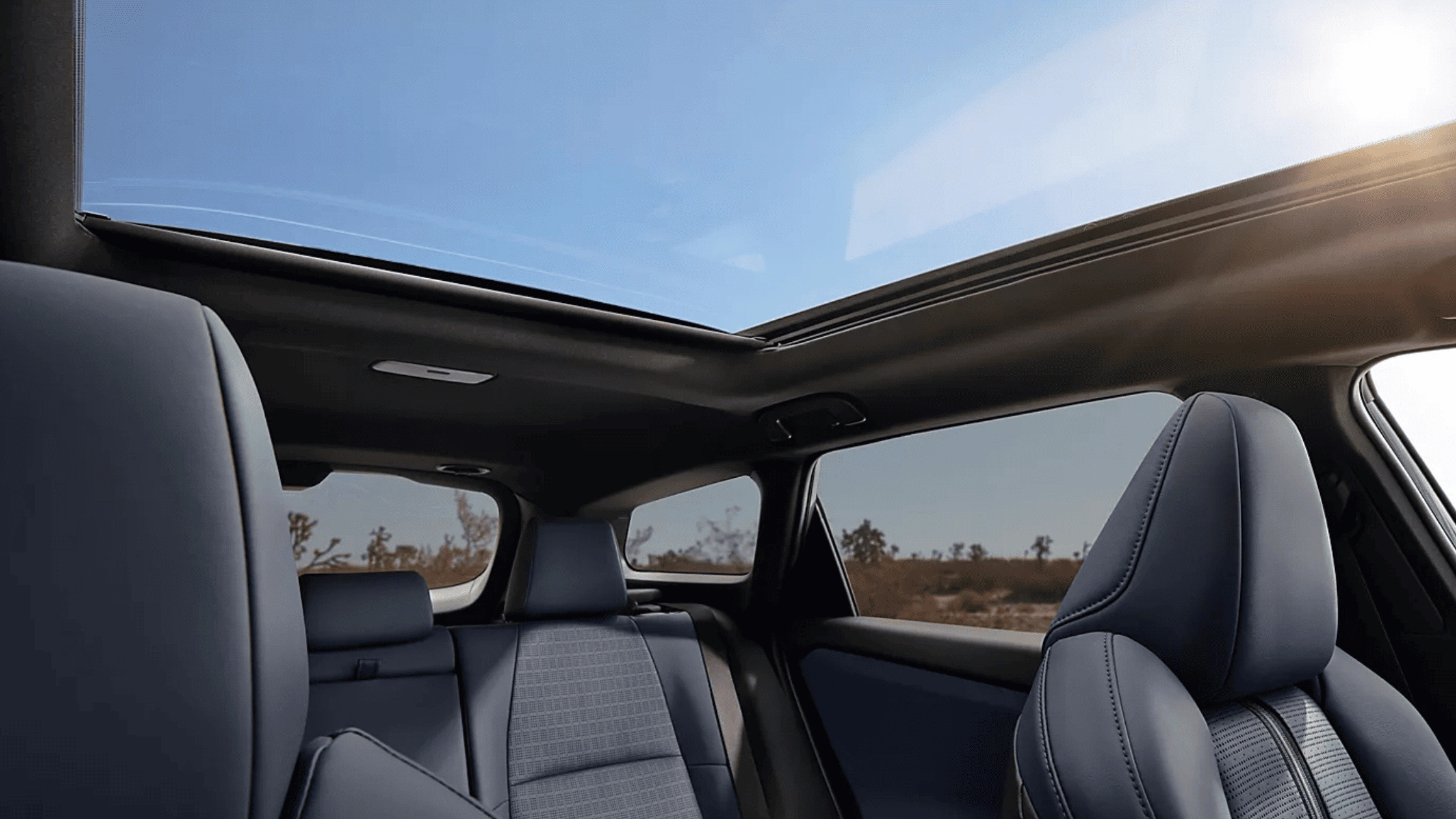 2026 Subaru Trailseeker interior showing blue front and rear seats with panoramic sunroof and wide desert landscape view through windows
