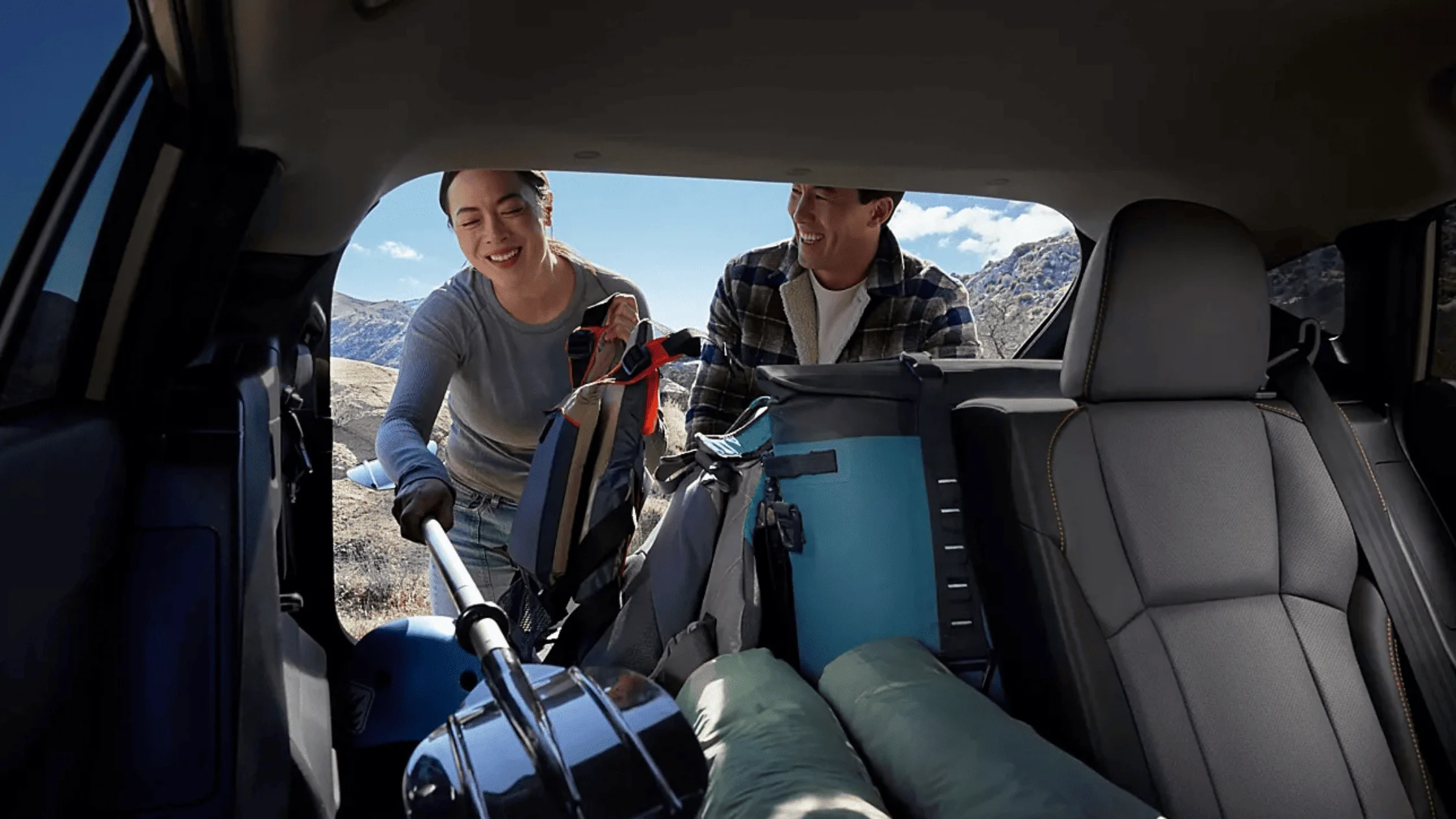 2026 Subaru Outback Wilderness cargo area loaded with camping gear including sleeping bag and trekking poles with rear hatch open in a desert setting