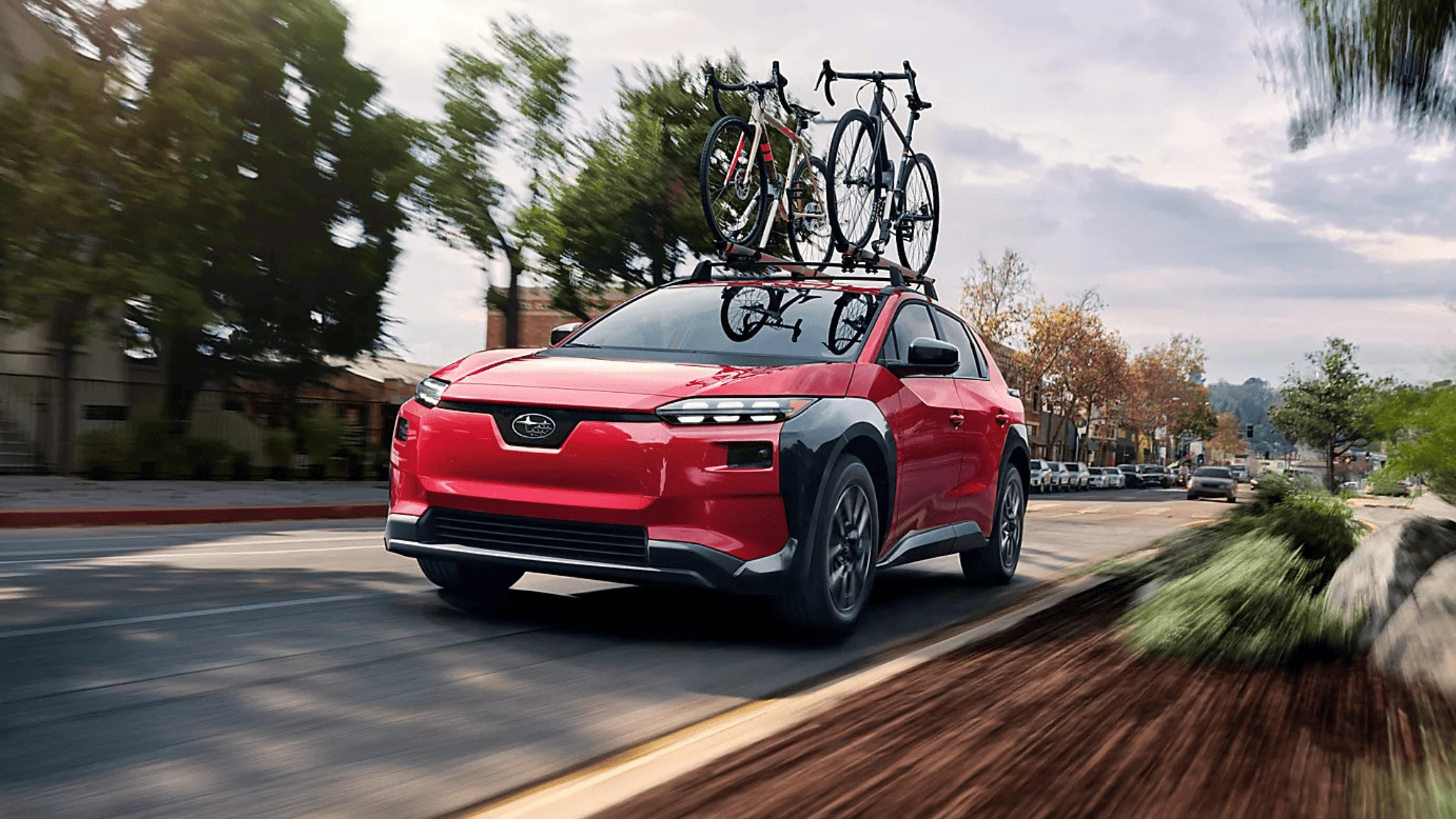 2026 Subaru Solterra electric SUV in red with roof-mounted bike rack carrying two bicycles driving through urban street in Pueblo CO