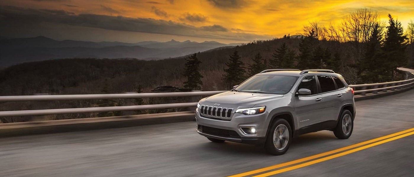2019 Jeep Cherokee driving down street during sunset