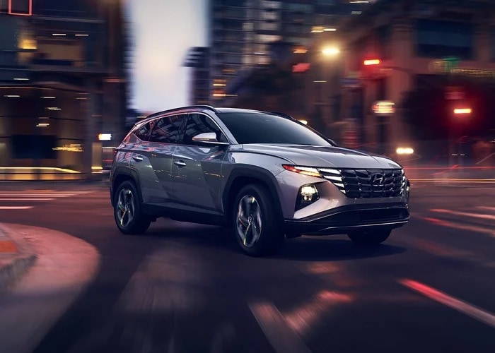 Grey 2023 Hyundai Tucson driving around in a lit up city at night