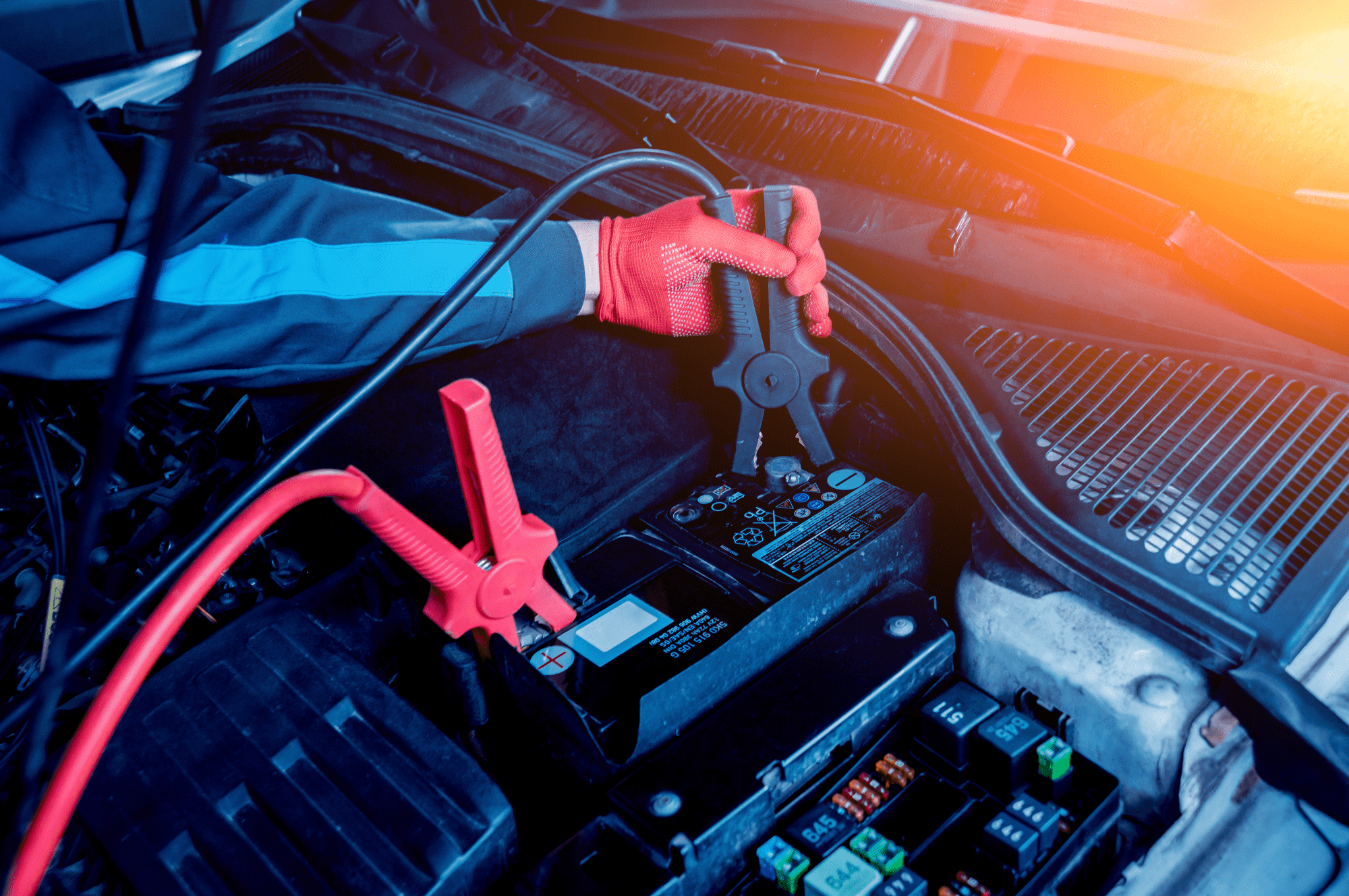 A service technician putting a jumper cable on a car battery