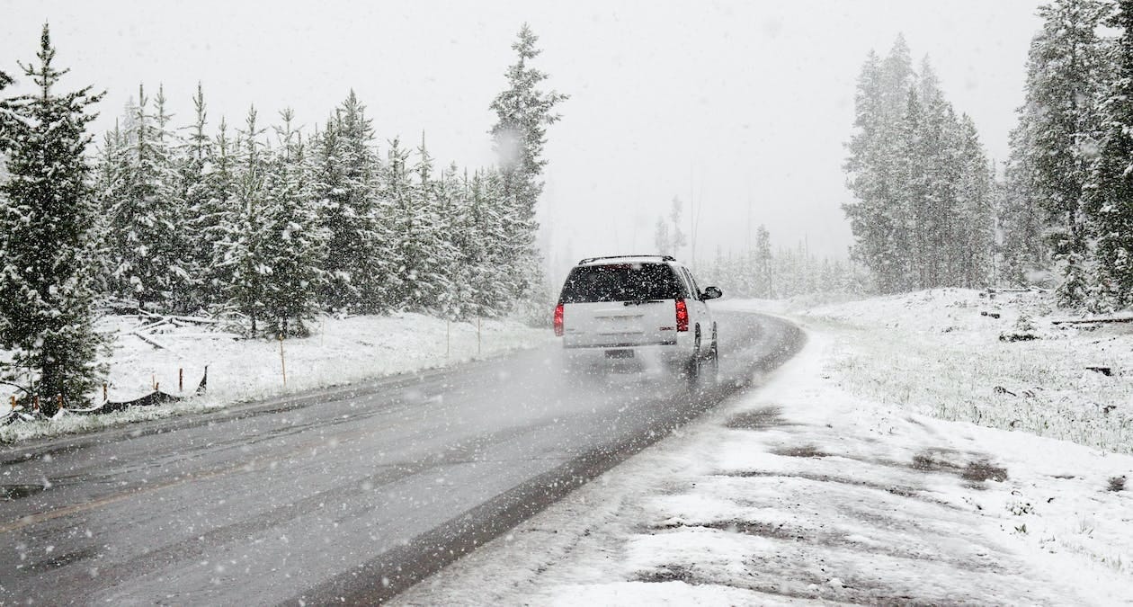  White SUV driving in a snowy and wooded area
