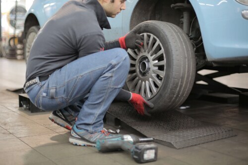 man changing tire on blue sedan