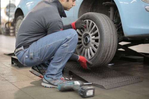 man changing tire on blue sedan