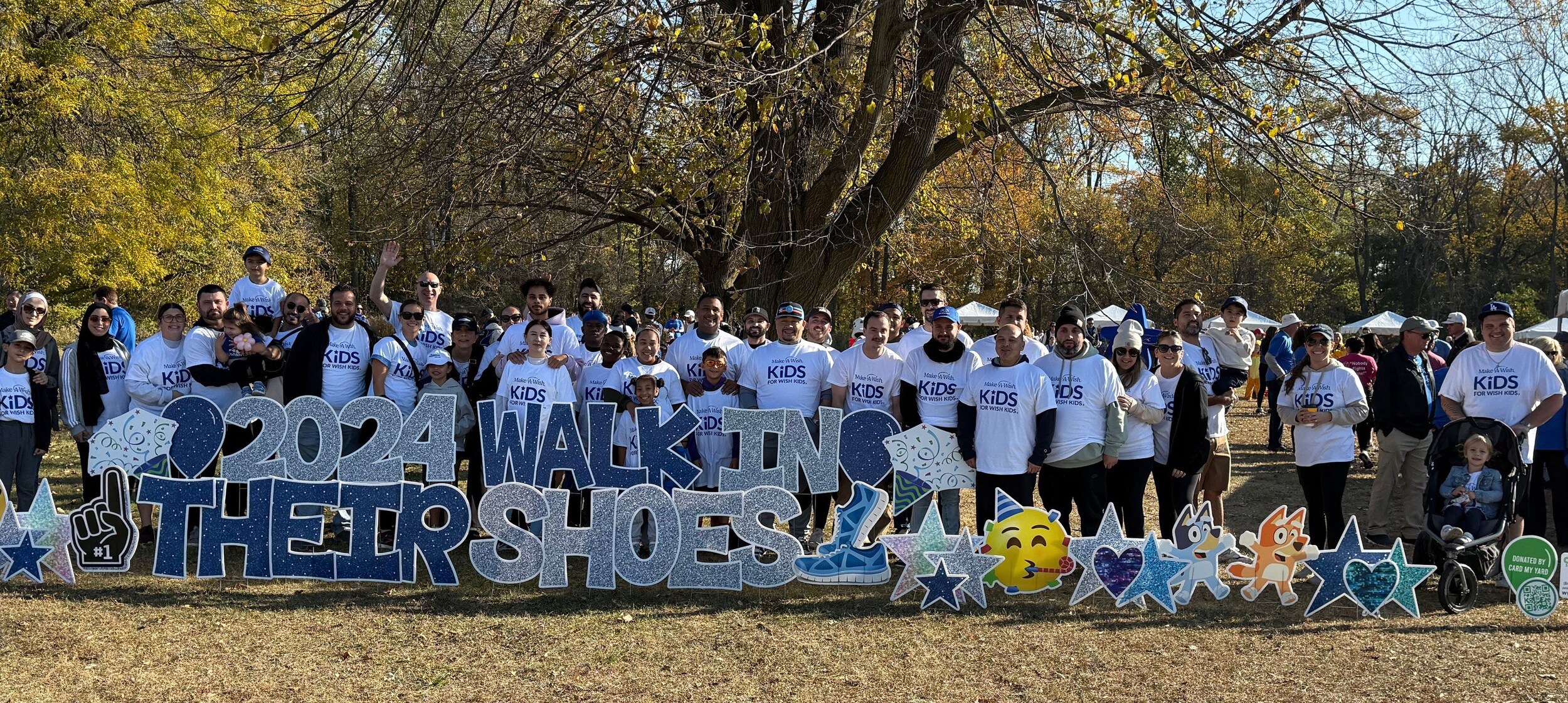 Group of people walking for charity holding a sign that reads 2024 Walk in their Shoes