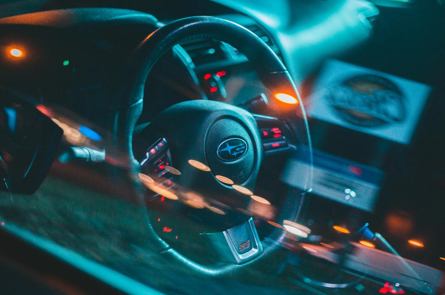 close-up view of a subaru steering wheel with city lights reflecting on the window 