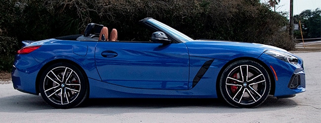 Side view of a blue BMW Z4 convertible with red brake calipers, top down, parked near a natural backdrop