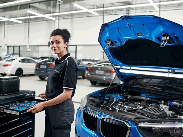BMW technician pulling tools from drawer beside open engine bay of a blue BMW