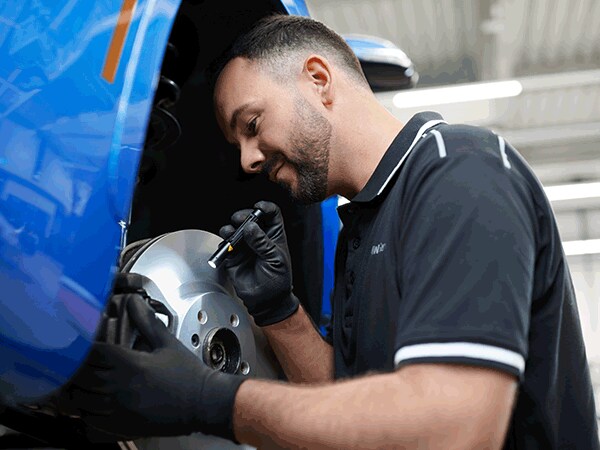 BMW service specialist carefully inspecting a brake rotor assembly on a vehicle in the shop