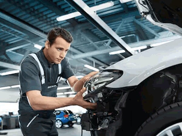 BMW technician replacing or adjusting front headlight unit on a vehicle in the service center