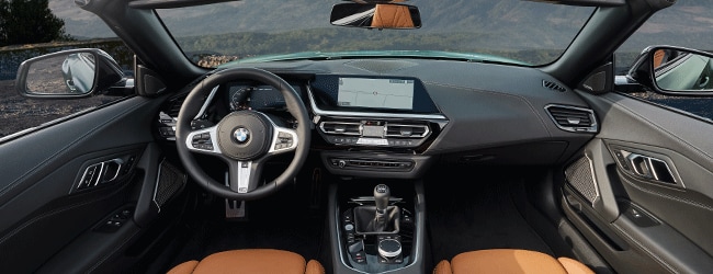 BMW Z4 convertible interior with manual transmission, orange seating, and scenic mountain view in background