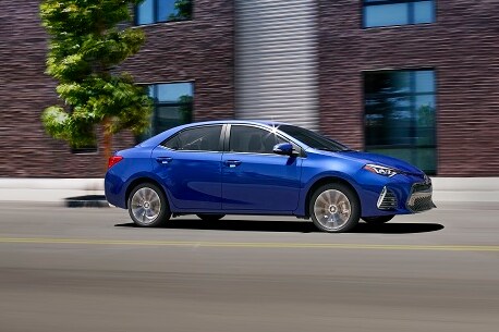 Blue Toyota Corolla on a city street with buildings made of brick