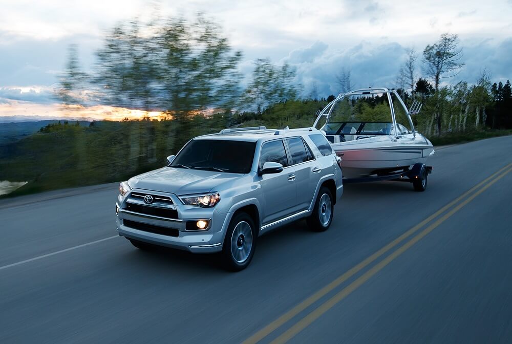 Gray Toyota 4Runner towing a boat on a suburban street with trees along the side.