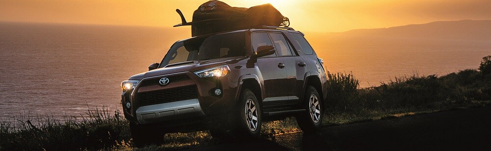 Red Toyota 4Runner with a sack on top near a lake trimmed with grass