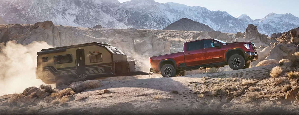 2024 GMC Sierra HD towing a trailer in an off-road setting