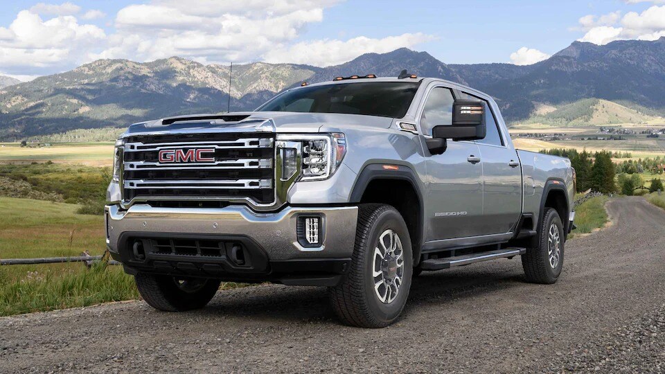 White 2023 GMC Sierra 2500 HD parked on a gravel road in front of the mountains