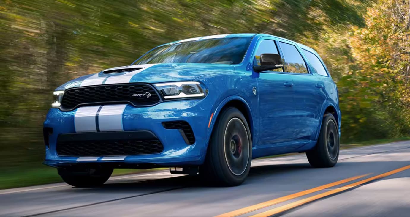 Front and side view of the 2024 Dodge Durango driving past trees