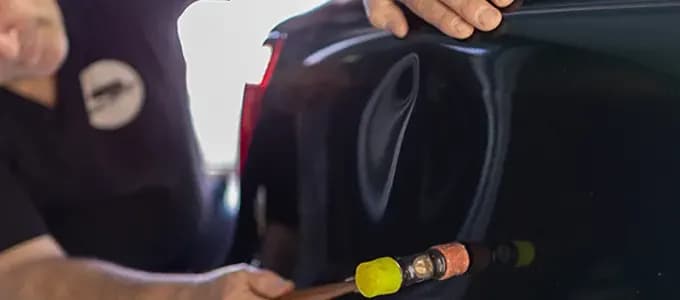 Autobody mechanic repairing dent in vehicle