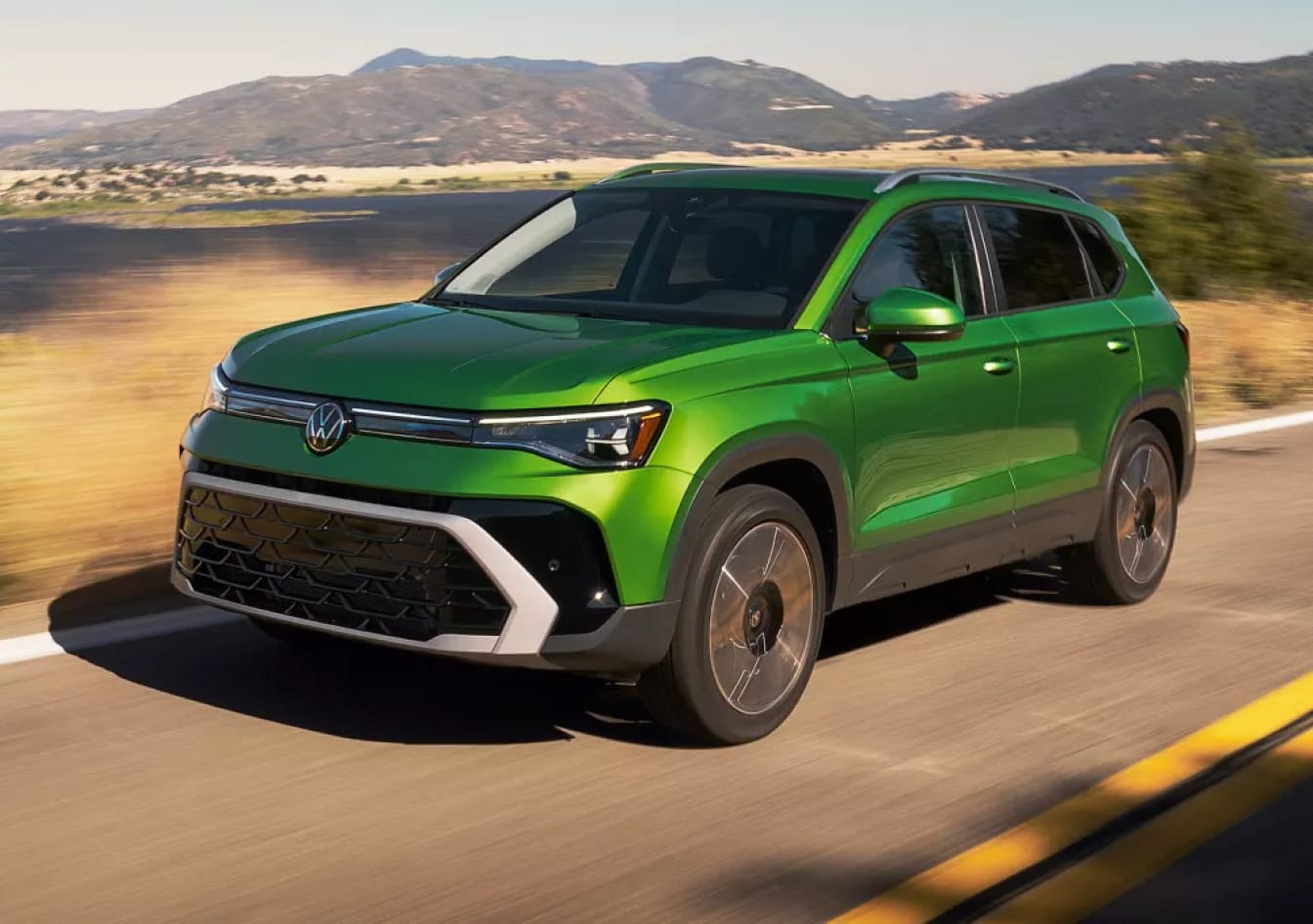 Green Volkswagen SUV driving on a road with mountains in the background.