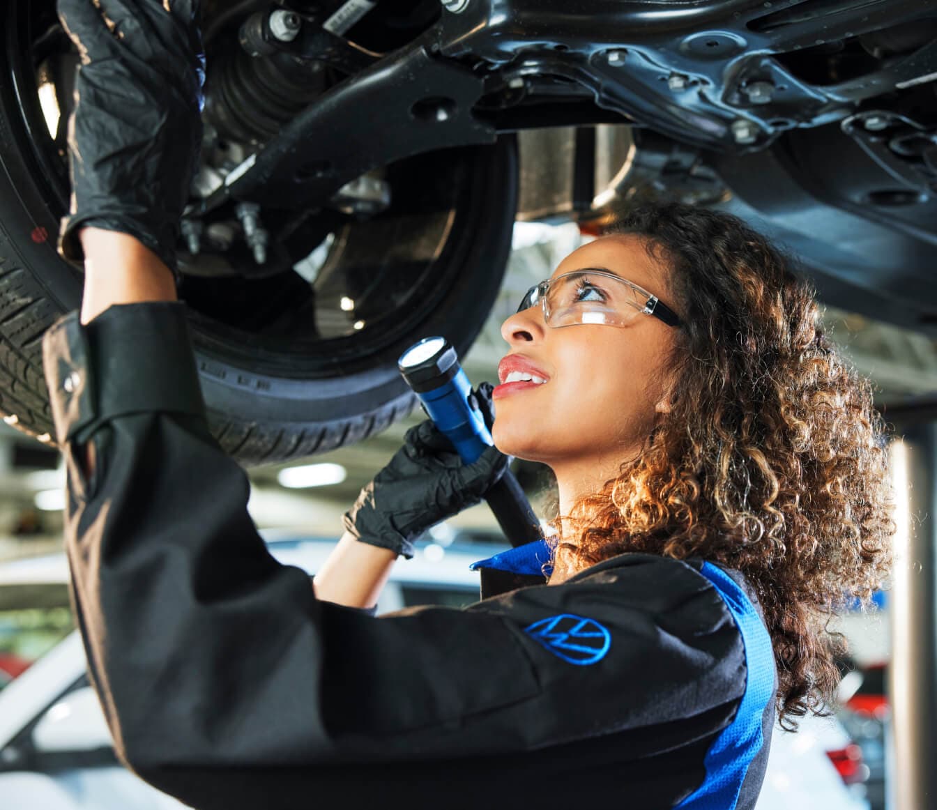 Volkswagen technician inspects the undercarriage with a flashlight for signs of a coolant leak in a service bay.