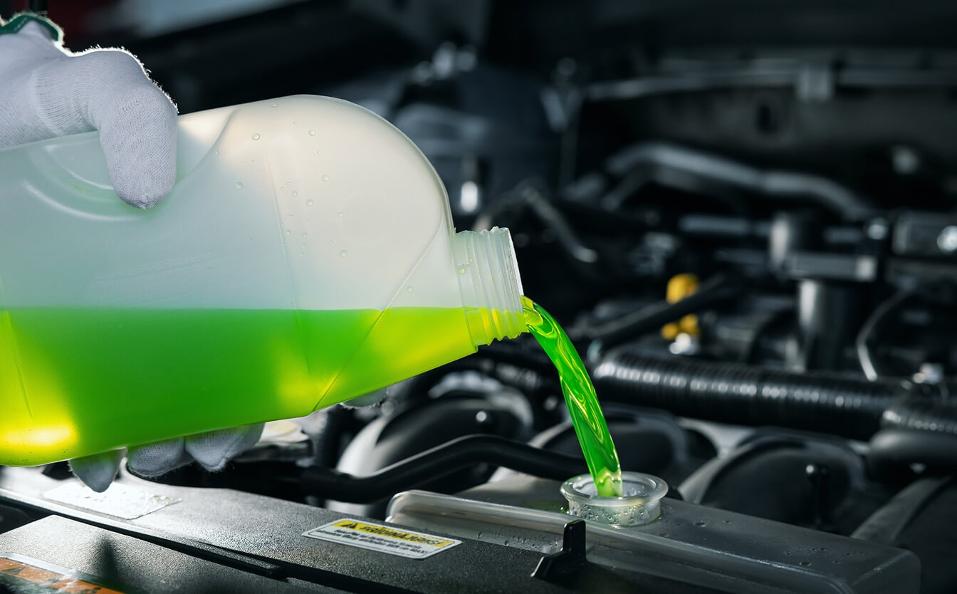 Green engine coolant is poured into a vehicle coolant tank reservoir under the hood during maintenance.