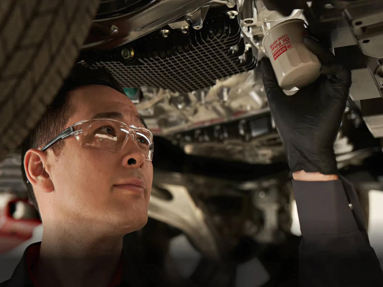 Automotive technician wearing glasses working on car engine repair in professional garage workshop