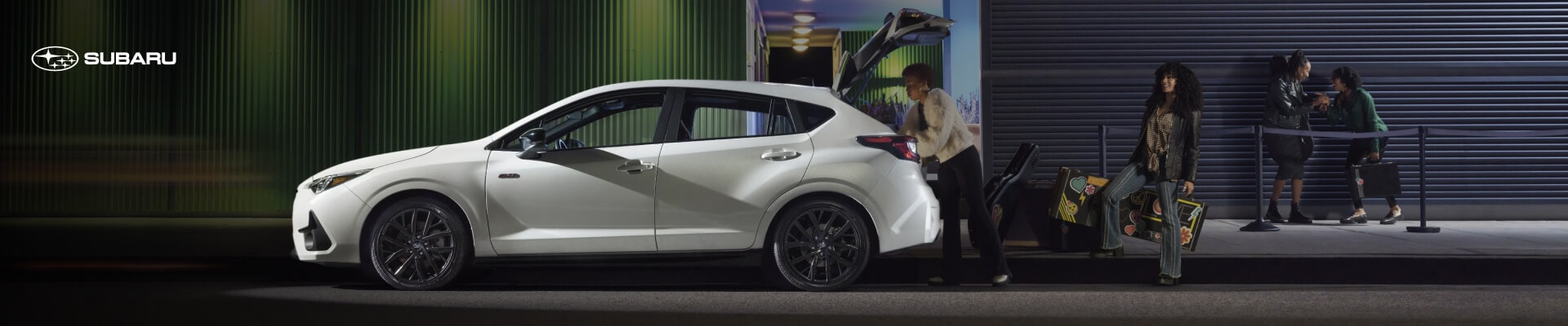 Subaru Impreza RS with open hatch being loaded with luggage at night outside an urban building.
