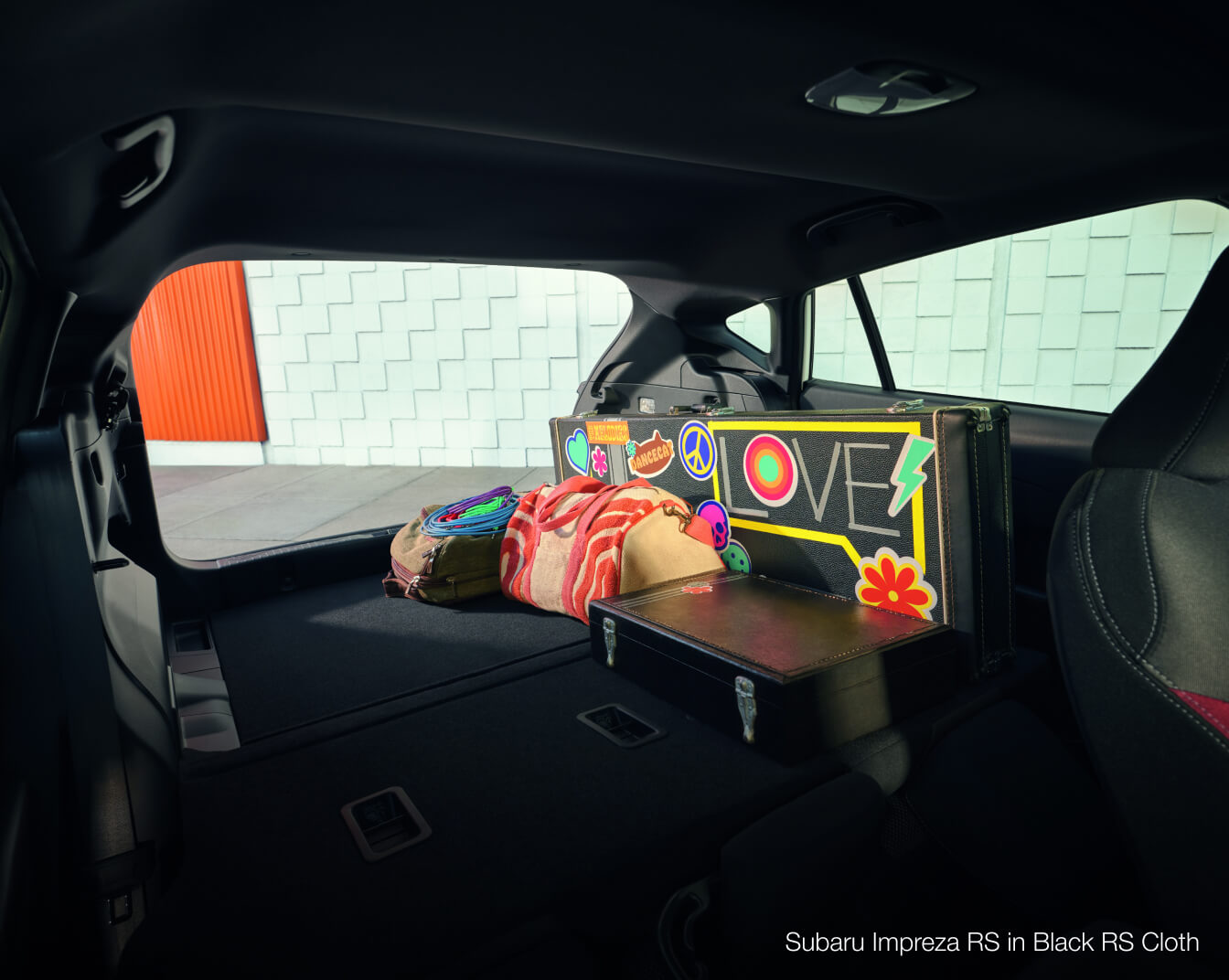 Subaru Impreza RS cargo area with folded rear seats holding suitcases in an urban driveway.
