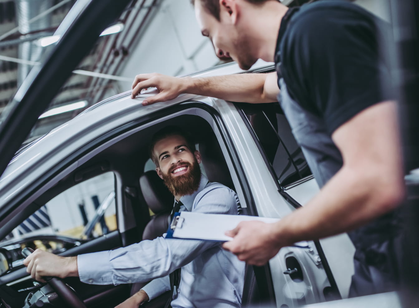 Service advisor speaking with a customer seated in a vehicle inside a service center.