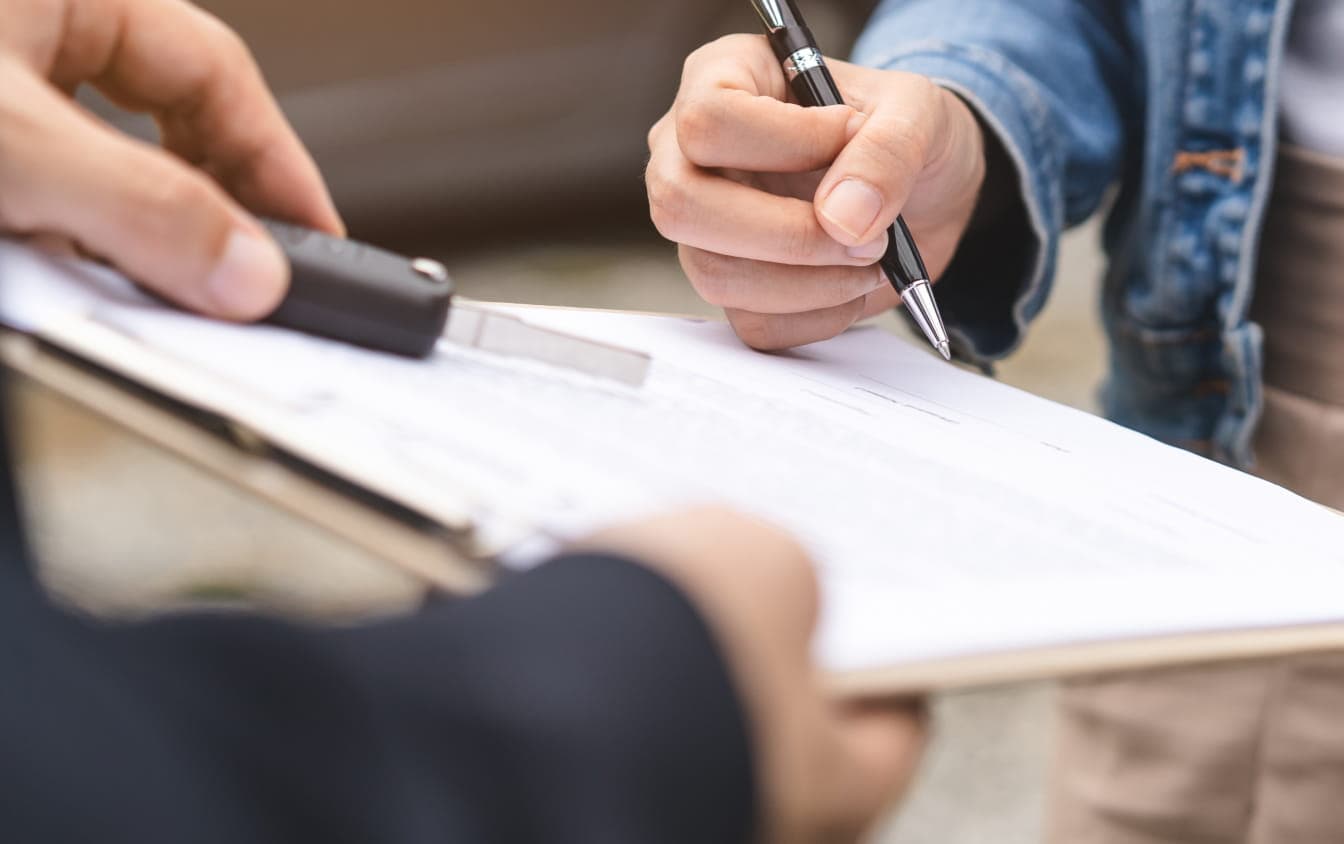 Customer signing paperwork while receiving a vehicle key during the purchase process.