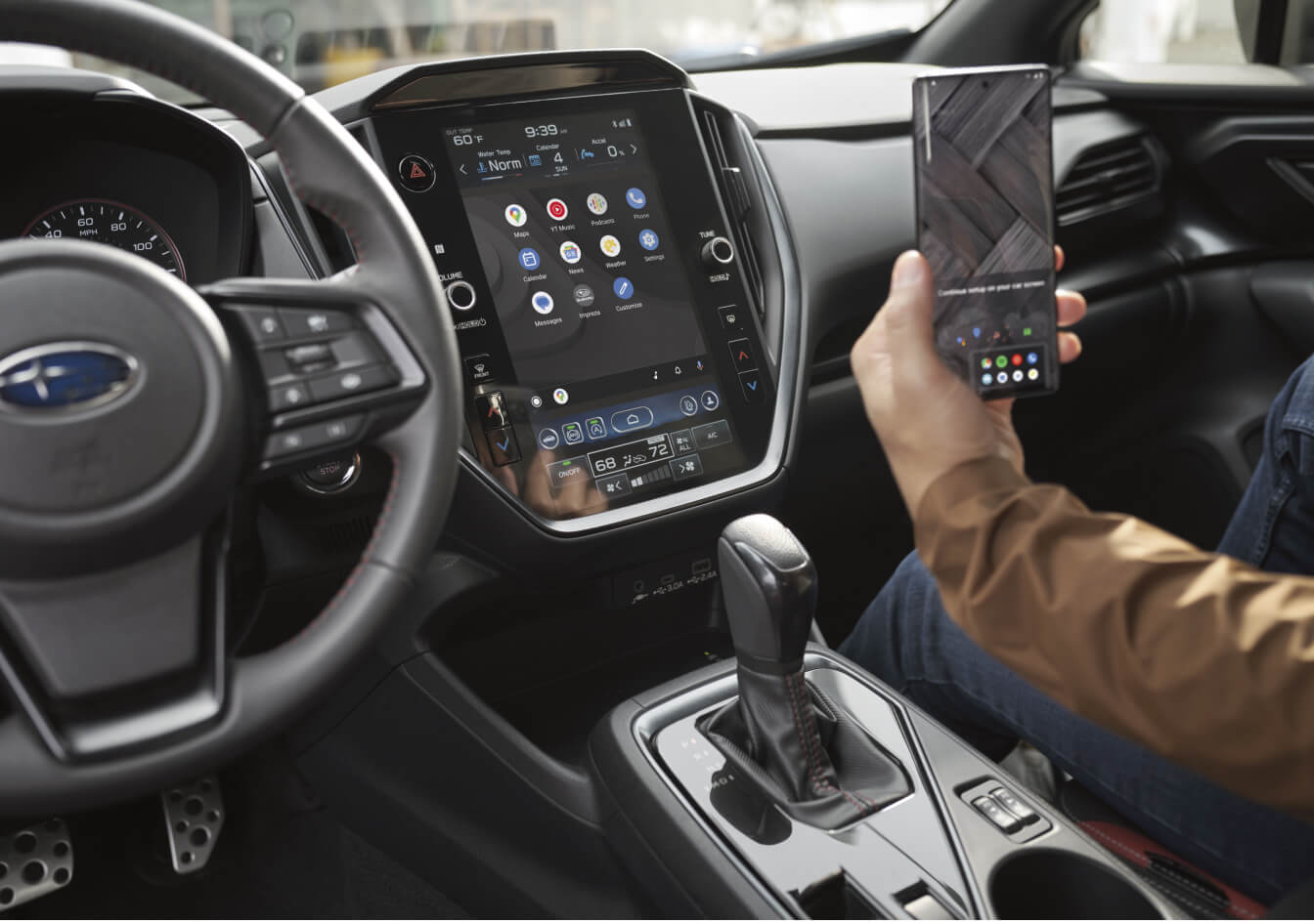 Subaru Impreza RS infotainment screen displaying apps next to a person holding a smartphone.