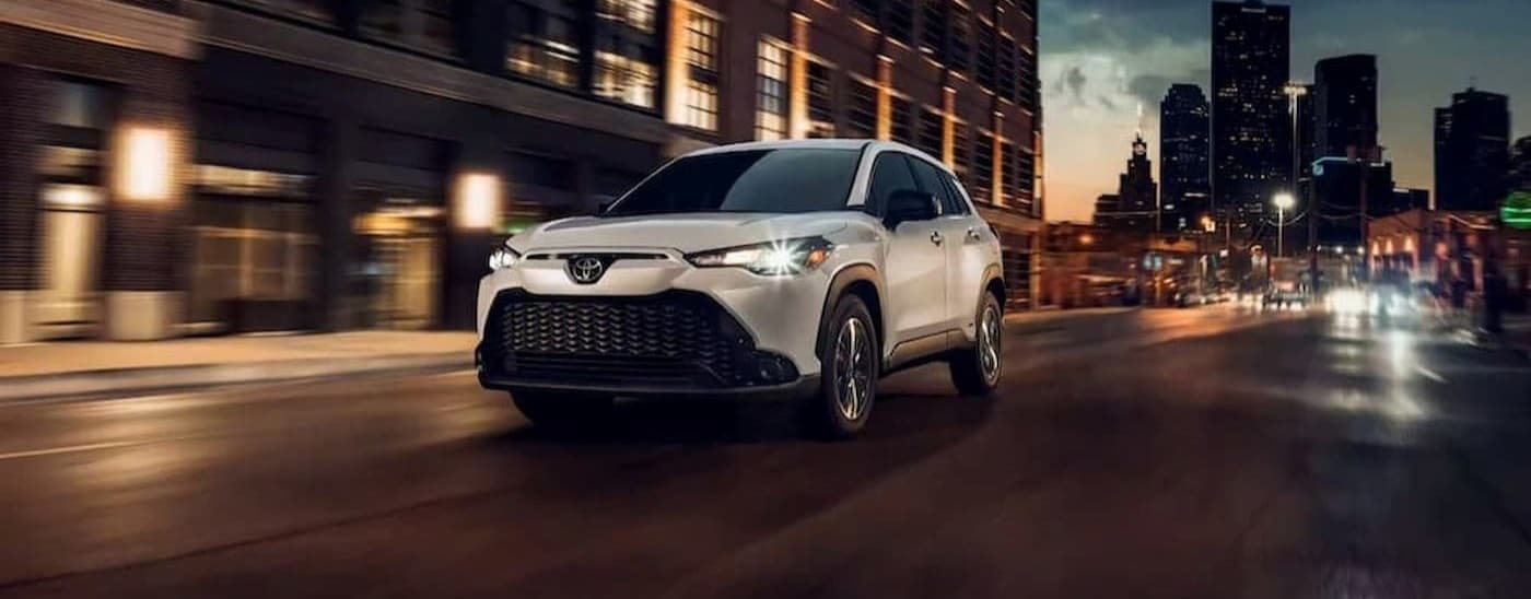 A white 2023 Toyota Corolla Cross is shown driving to visit a Toyota dealer near Madisonville.