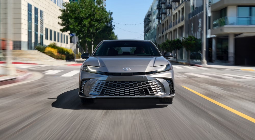 Head-on view of a silver 2025 Toyota Camry Hybrid XSE driving in a city.