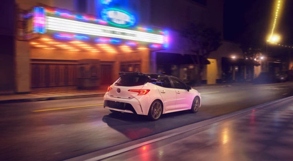 A white 2024 Toyota Corolla Nightshade is shown driving past a theatre.