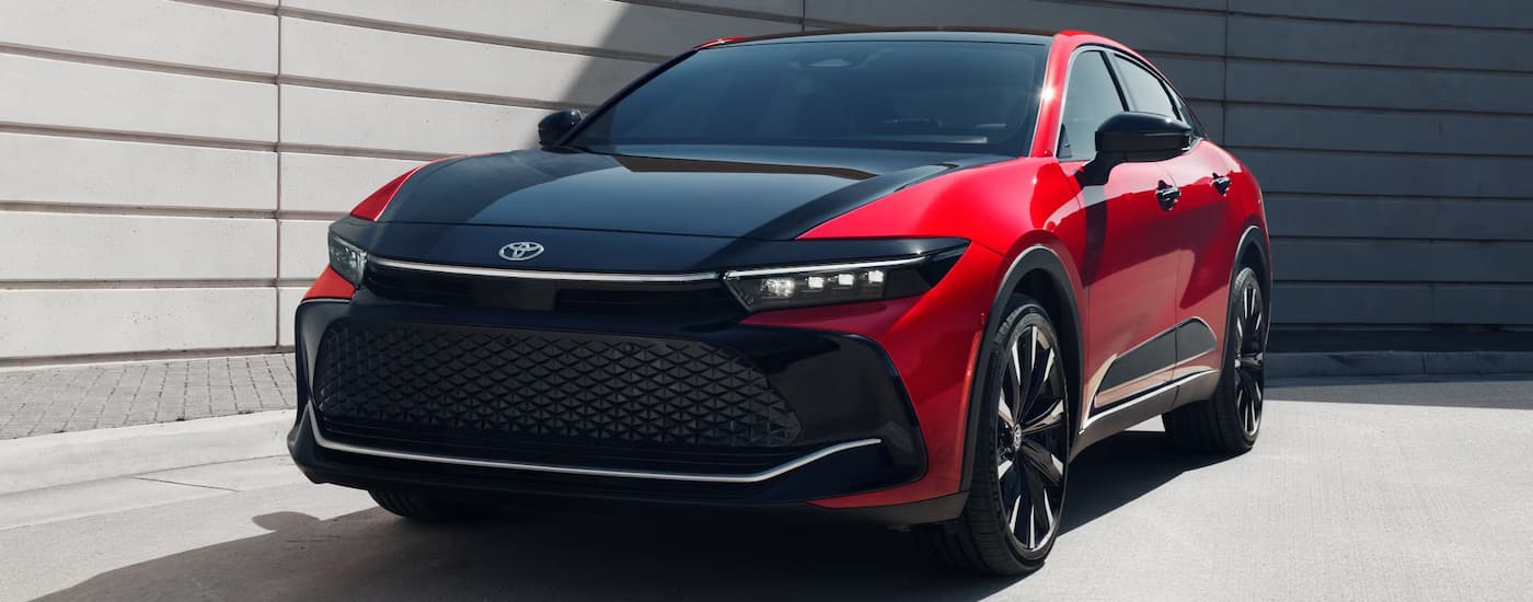 A red and black 2025 Toyota Crown Platinum parked near a concrete wall.