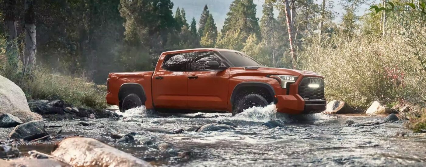A red/orange 2024 Toyota Tundra TRD Pro is shown driving though a creek.