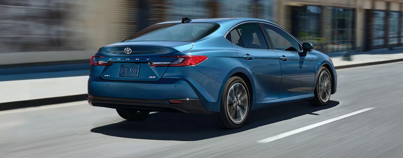 Rear view of a blue 2025 Toyota Camry Hybrid XLE driving downtown.