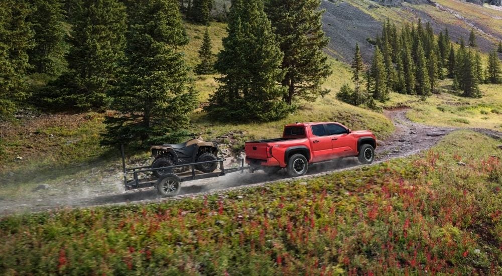 An orange 2024 Toyota Tacoma TDR Off-Road towing an ATV up a hill.