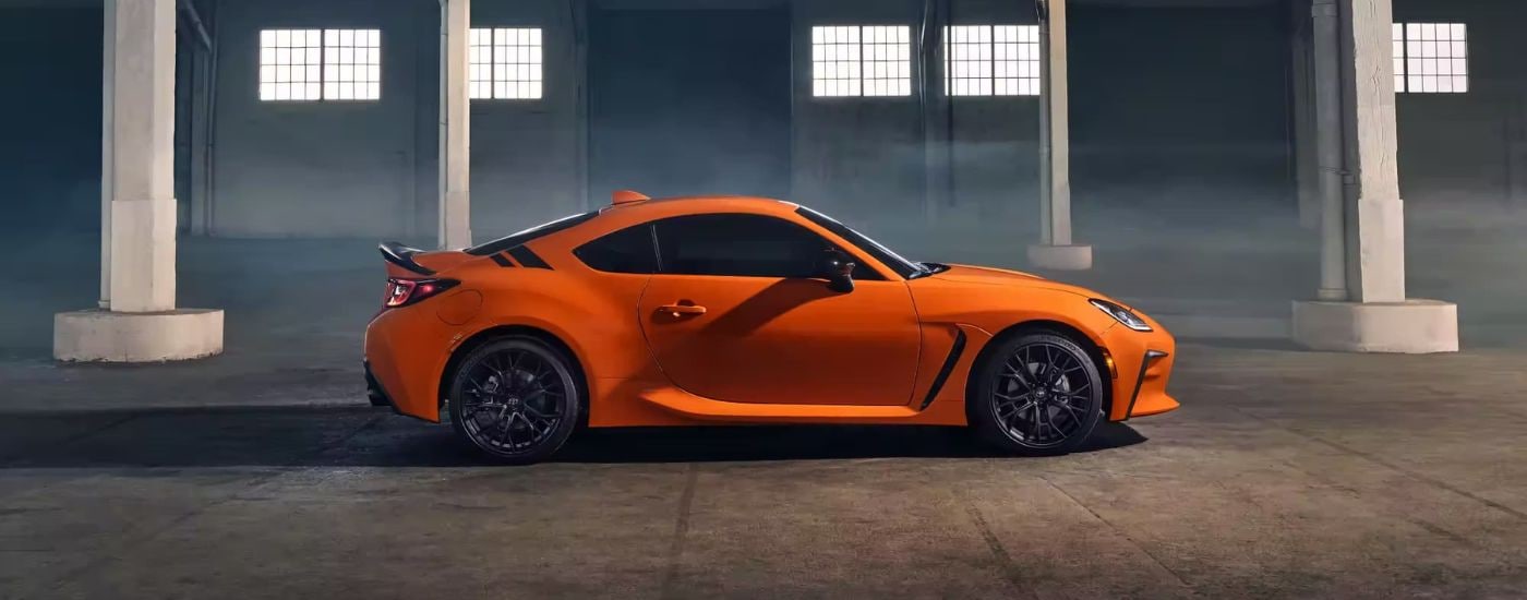 An orange 2023 Toyota GR 86 10th Anniversary is shown from the side parked in a warehouse.
