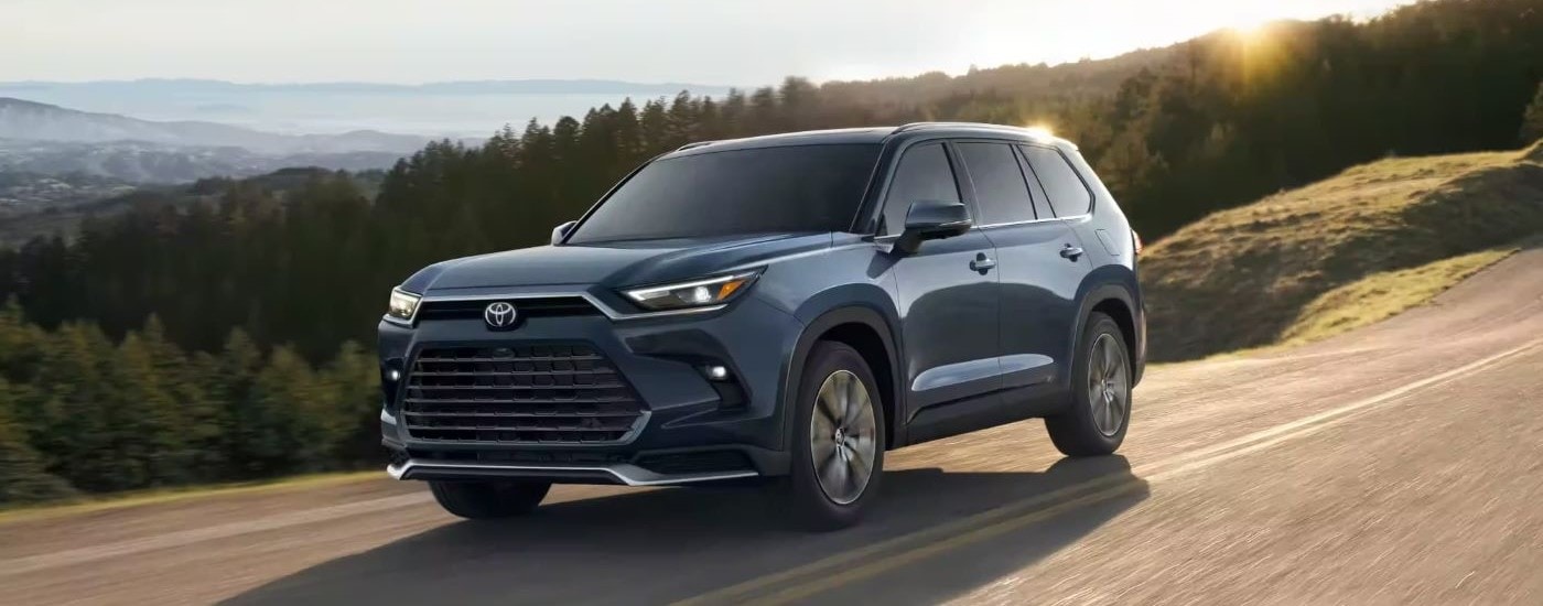 Blue 2024 Toyota Grand Highlander for sale near Madisonville driving on a tree-lined road