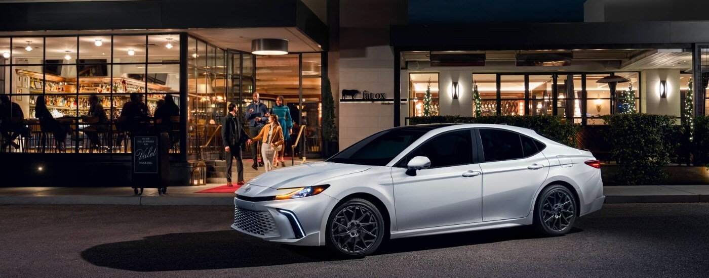 A white 2025 Toyota Camry is shown from the side after leaving a Toyota dealer near Russelville.